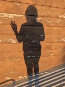 The shadow of a person against a timber wall in the early morning sunshine, with one hand raised as if waving